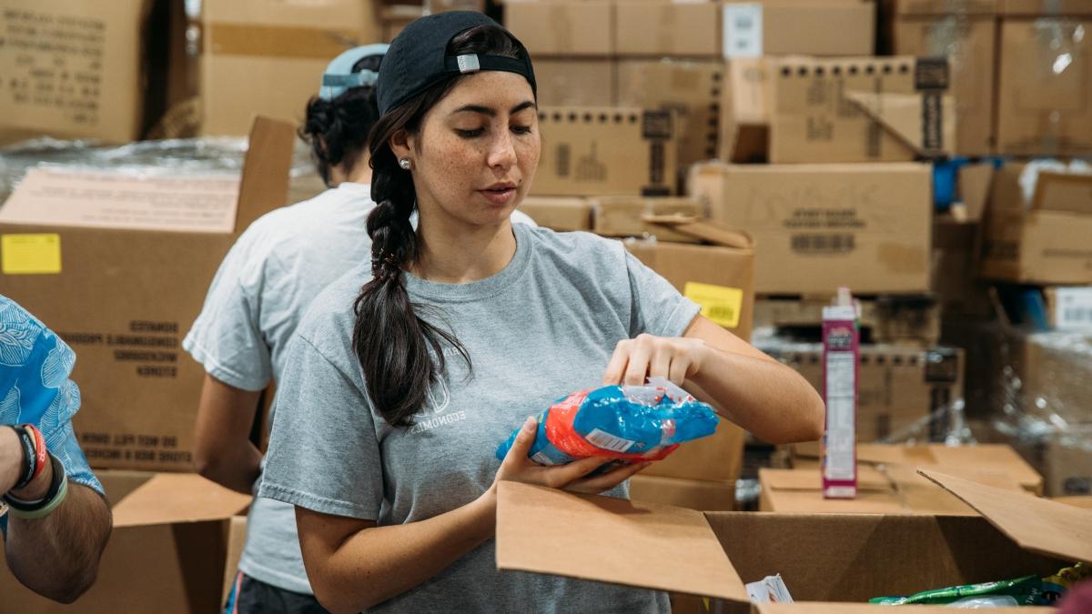 a woman volunteer packs supplies into a cardboard box on an assembly line